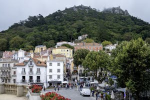 Vibrant street scene in Sintra, Portugal, showcasing colorful buildings and the Moorish Castle on a lush hillside.