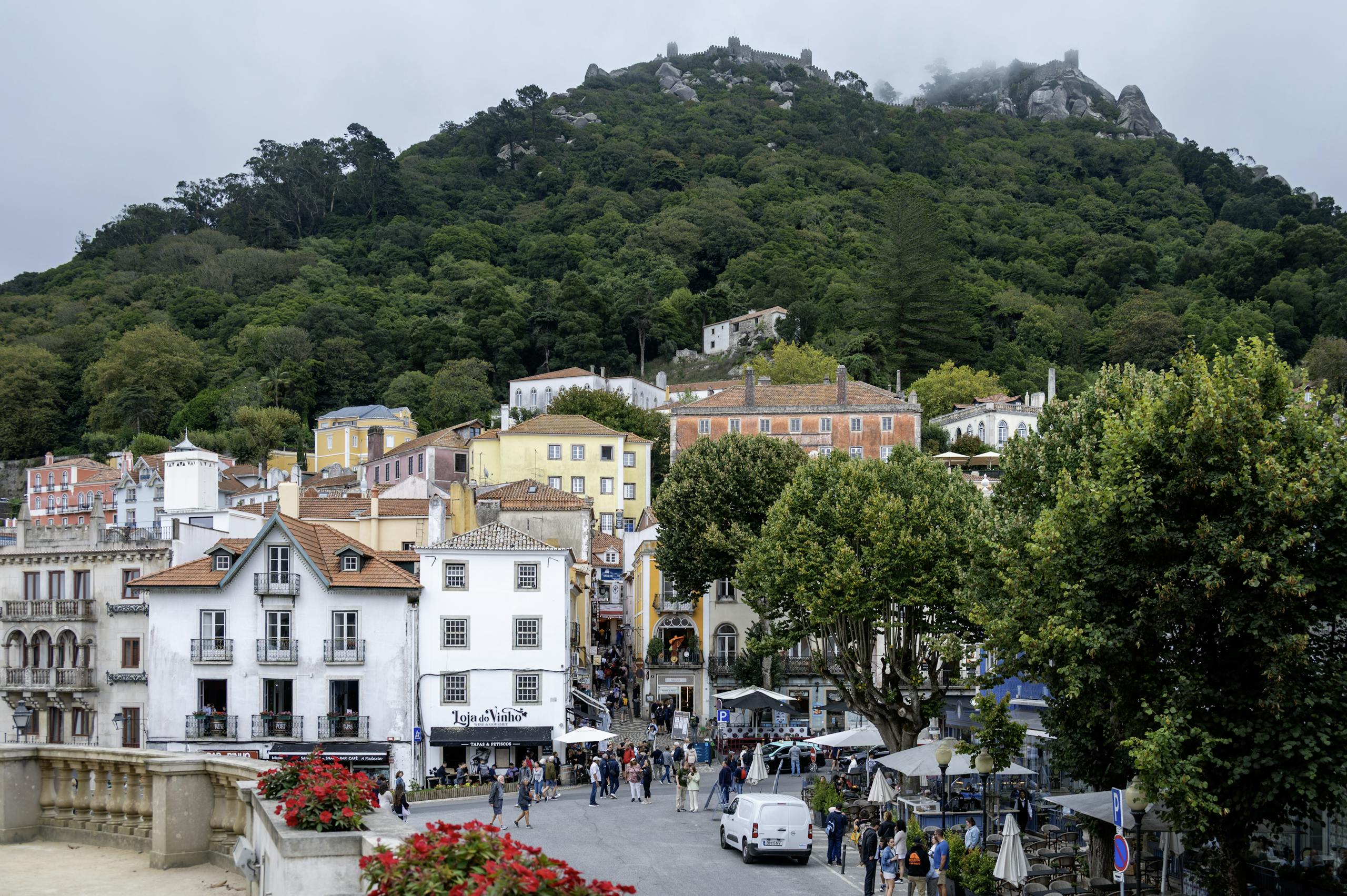 Vibrant street scene in Sintra, Portugal, showcasing colorful buildings and the Moorish Castle on a lush hillside.